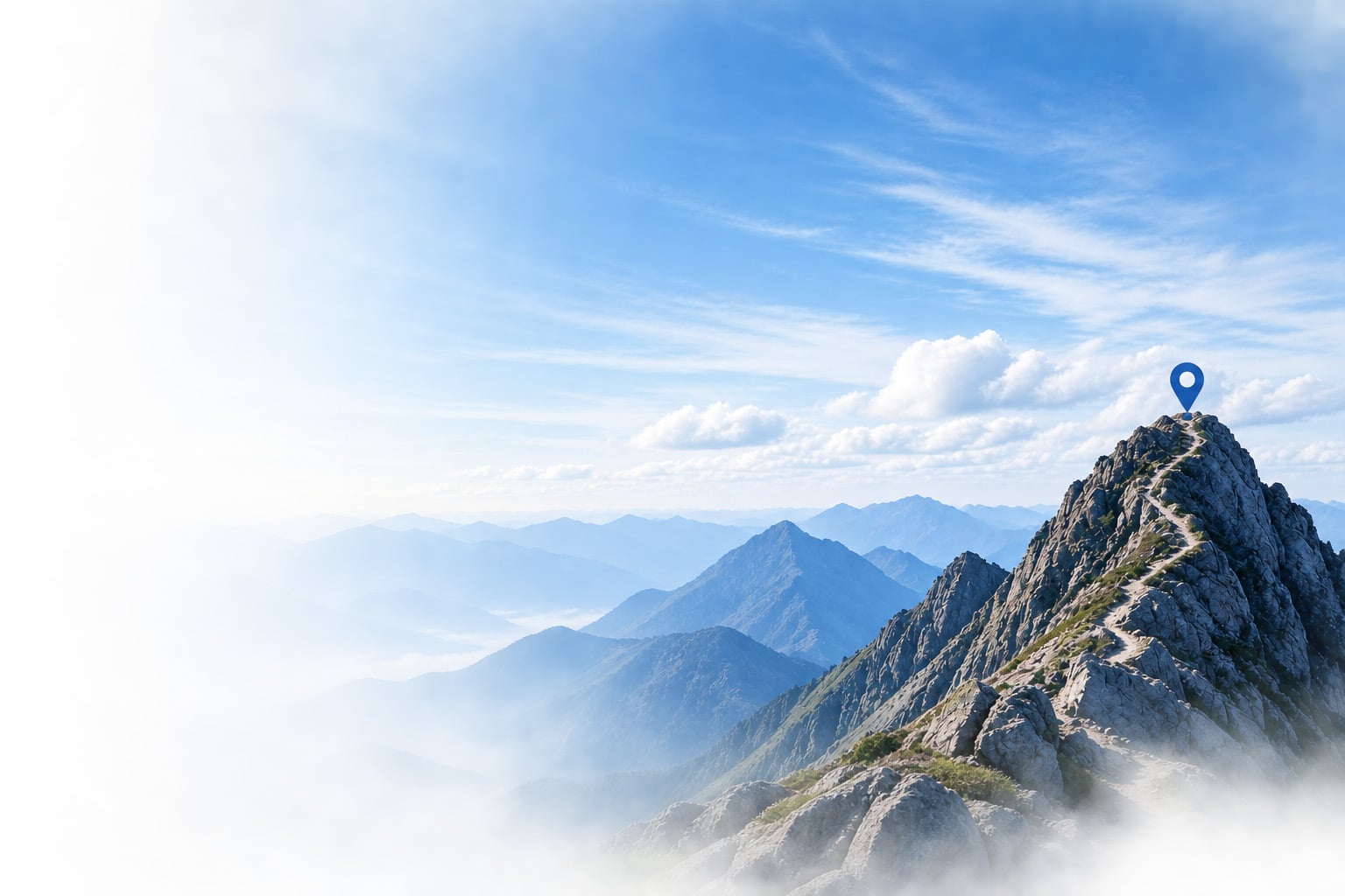 A trail winds up a rocky ridge to a pin marker at a mountain summit above the clouds